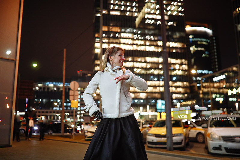夜晚舞蹈：穿着温暖外套的女性在城市街道上享受巴查塔舞，感受健康与快乐。图片素材