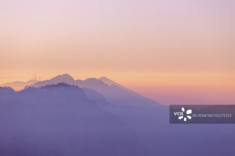 日出时的山脉风景，柔和的粉色和橙色与雾气缭绕的山峰层次交融。图片素材
