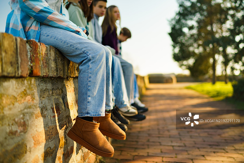 一群朋友把腿挂在砖墙上放松。图片素材