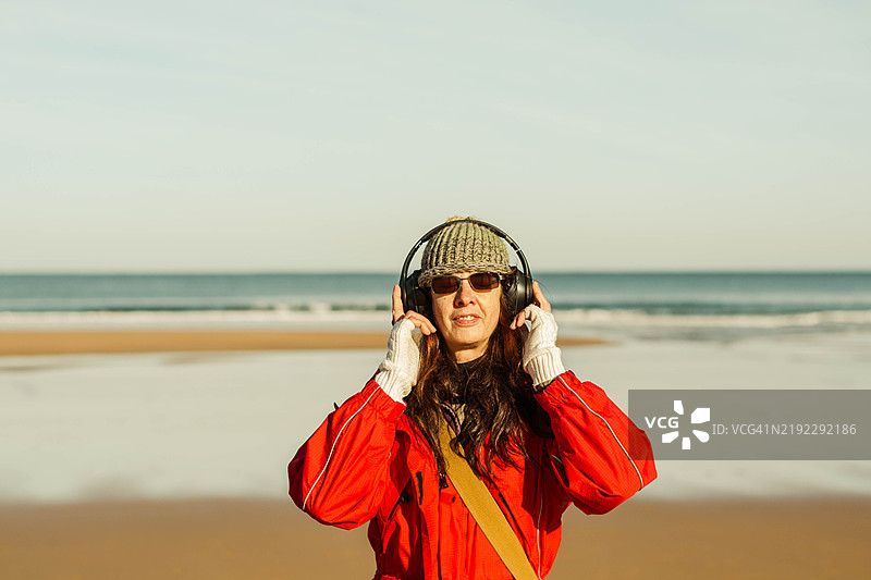 冬天在海滩上戴着耳机听音乐的女人图片素材