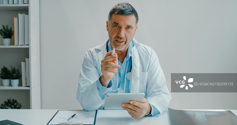 穿着实验室外套的资深医生使用数字平板进行远程医疗咨询，在临床办公室讨论医疗信息。医疗保健。图片素材