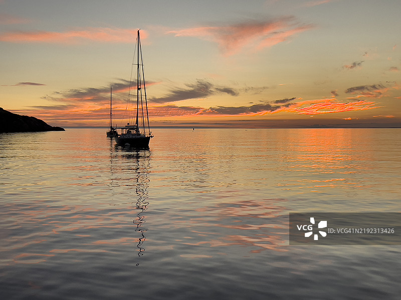 日落时分的魔幻光线，帆船剪影与平静海面上的倒影图片素材