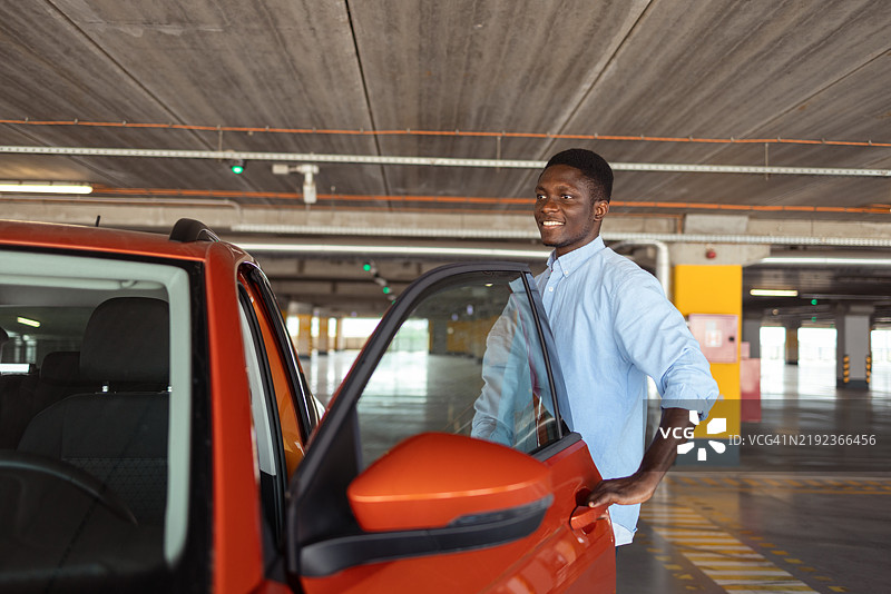 快乐的非裔美国男子在公共车库打开他的车门图片素材