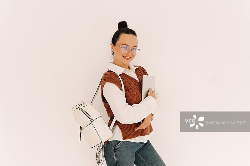 一名大学生穿着衬衫、背心和眼镜，手持笔记本电脑，利用无线技术在线工作，站在孤立的白色背景上。留白处可供添加文字。图片素材