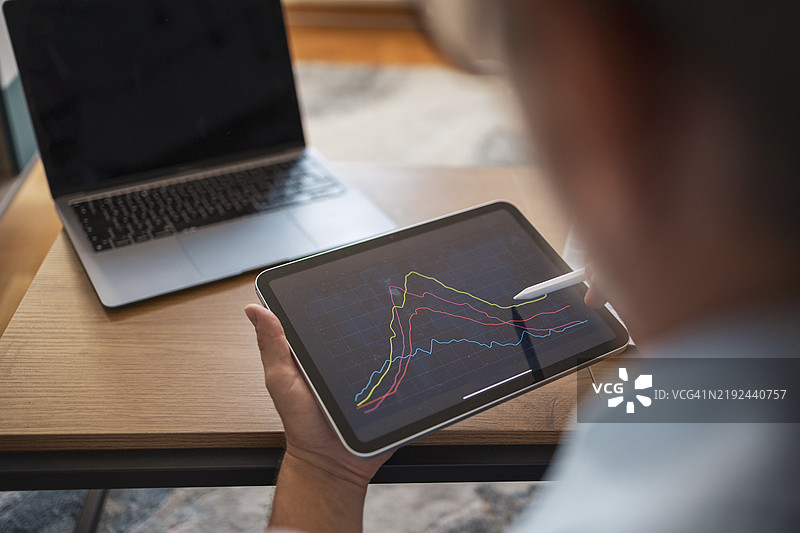 成熟男性在家中的书桌上分析平板电脑上的财务图表图片素材