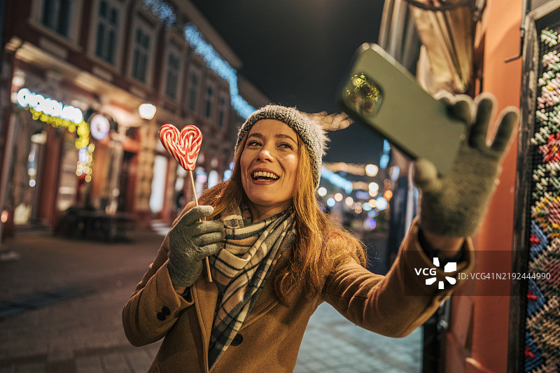 美丽的女人在城市中享受圣诞夜并使用智能手机的肖像图片素材
