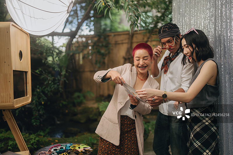 女性朋友在婚礼上享受乐趣，站在照片亭前拍照并选择将其保存在手机上。图片素材