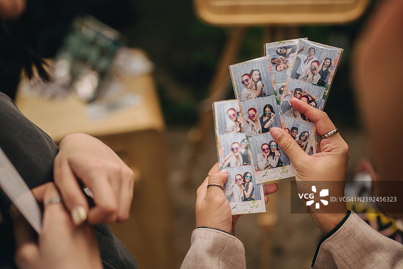 女性朋友在婚礼上享受乐趣，站在照片亭前拍照并选择将其保存在手机上。图片素材