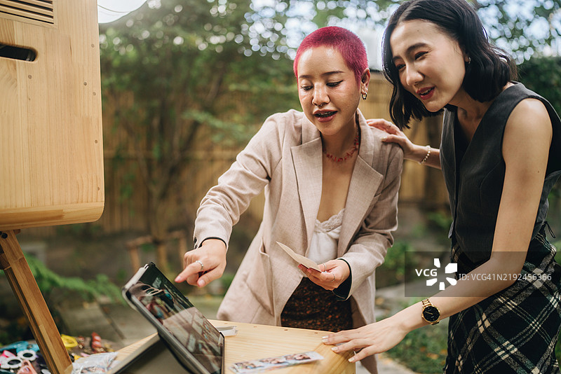 女性朋友在婚礼上享受乐趣，站在照片亭前拍照并选择将其保存在手机上。图片素材