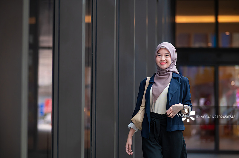 年轻的穆斯林女商人提着手提包走在现代办公大楼里图片素材
