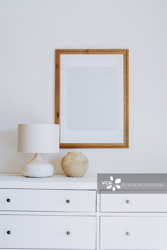 极简主义室内设计，白色梳妆台上摆放着空的木框、陶瓷花瓶和灯具。装饰细节。木框、花瓶和灯具呈自然色调。样板创意。时尚的极简室内。图片素材