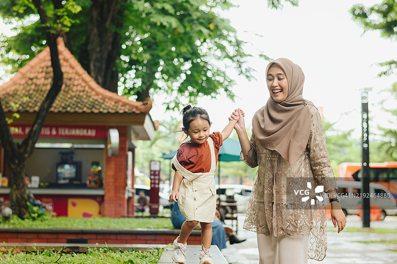 年轻的亚洲母亲和女儿在郁郁葱葱的户外公园中亲密互动图片素材