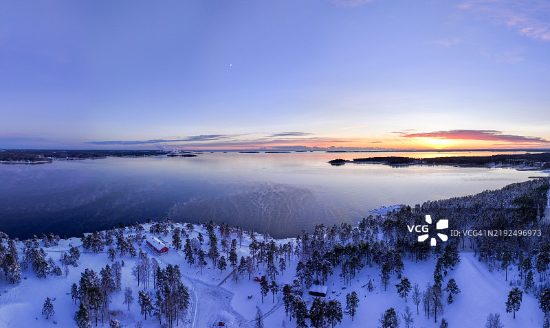 宁静的雪景，夕阳映照在斯堪的纳维亚森林和湖泊上图片素材