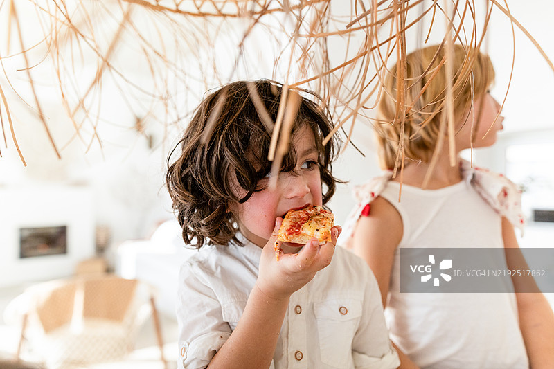 两个孩子在家里吃披萨，背景是藤编装饰。图片素材