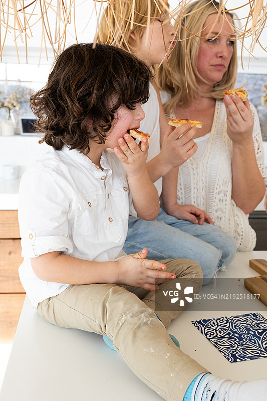 母亲和孩子们在厨房桌子上一起吃自制披萨图片素材