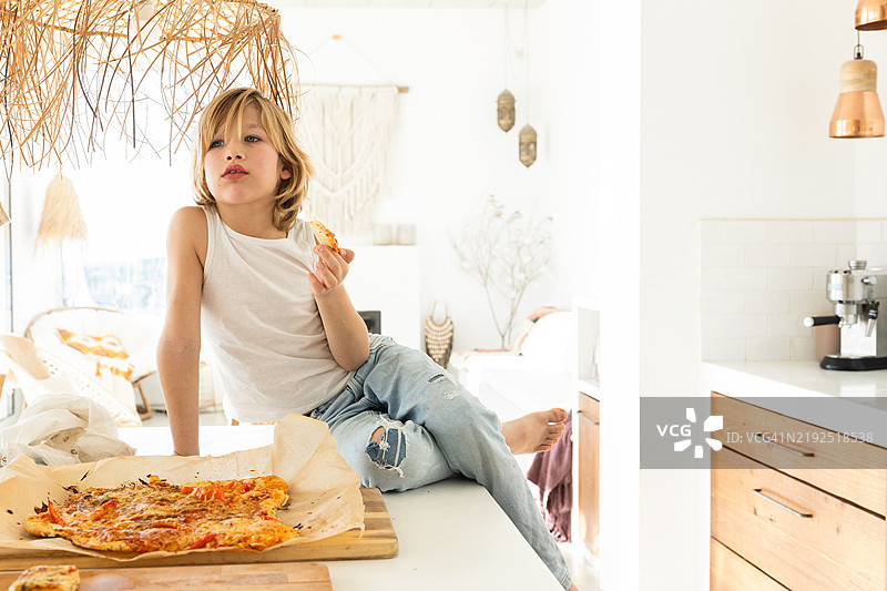 年轻男孩在现代厨房里吃自制披萨图片素材