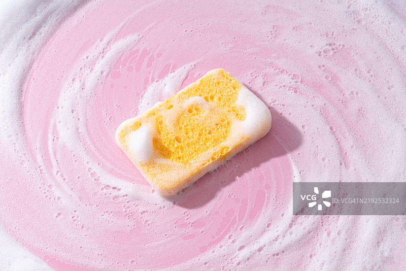 粉色背景上的黄色海绵与肥皂泡沫一起清洁图片素材