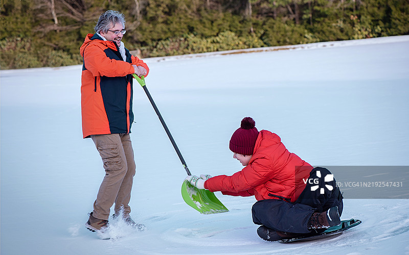 冬季适应性运动在冰冻湖面上。53岁的父亲使用滑雪器引导自闭症儿子进行雪地活动。图片素材