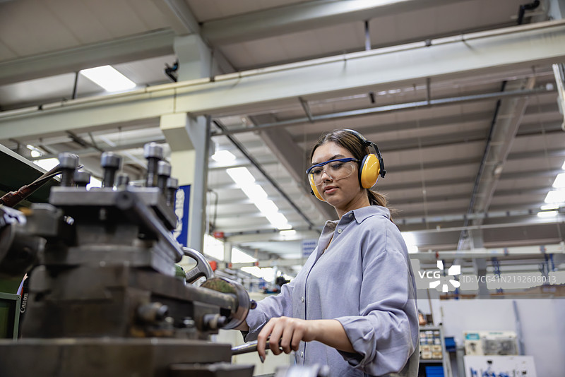 年轻的车床女工在工厂中使用铣床。图片素材