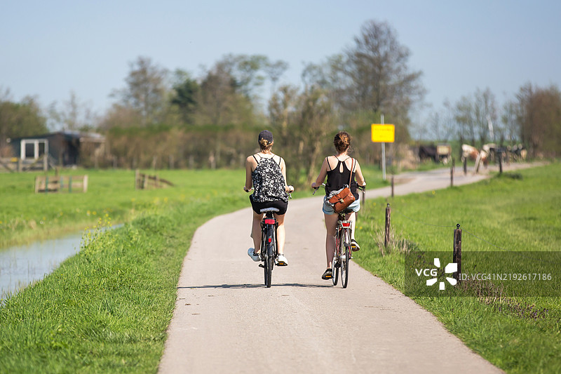 两位无法辨认的年轻女性在自然中的自行车道上骑行图片素材