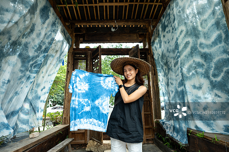 一位年轻的中国女性戴着竹帽，手持扎染布料，使用传统的中国染色技艺。图片素材