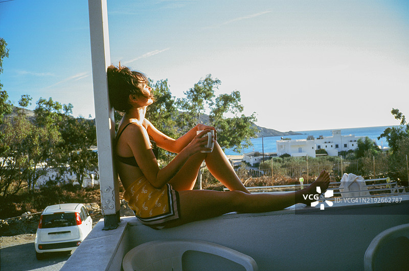 女人在阳台上眺望海边，体验希腊岛屿之旅。图片素材