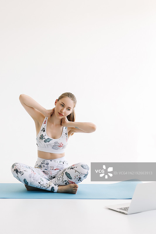 一位运动女性在健身垫上锻炼，手里拿着可回收水瓶，正在观看笔记本电脑上的健身视频。一位穿着运动服的健身教练在白色背景下通过科技进行在线训练。广告位。在线培训。图片素材