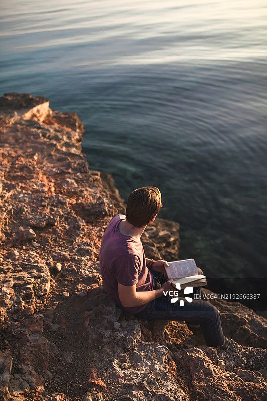 年轻男子在海边日落时阅读书籍图片素材
