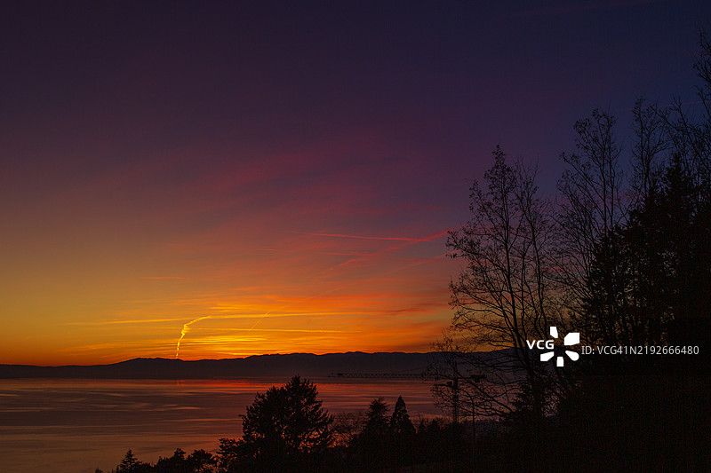 日落时分，湖面上空出现戏剧性的多彩天空，前景中有逆光的树木。图片素材