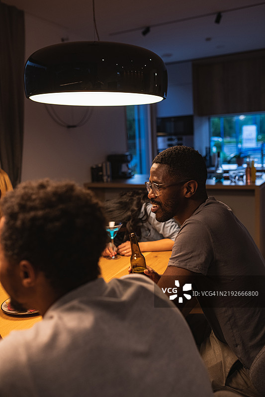 一位肤色较深的男子在夜晚与朋友聚会时手持啤酒的肖像图片素材