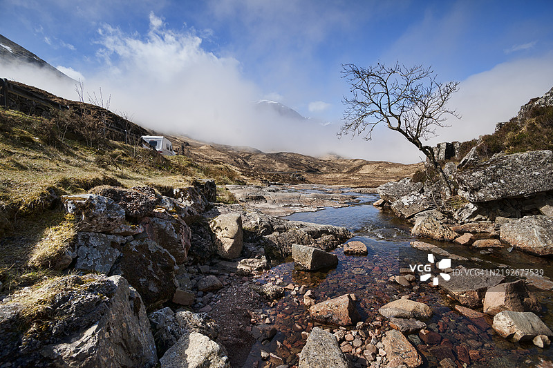 格伦科山脉的房车和溪流。从A82公路的“水会合”路边停车场附近向西北方向俯瞰格伦科山脉。格伦科，洛哈伯，高地地区，苏格兰，英国。图片素材