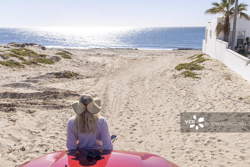 成熟的女性倚靠在海滩上的汽车上图片素材