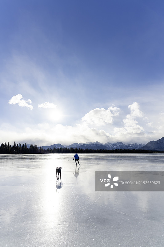 女人在冰冻的湖面上滑冰，身边有一只狗。图片素材