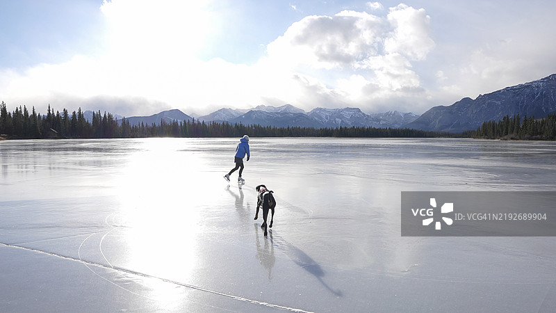 女人在冰冻的池塘上滑冰，身边有狗。图片素材
