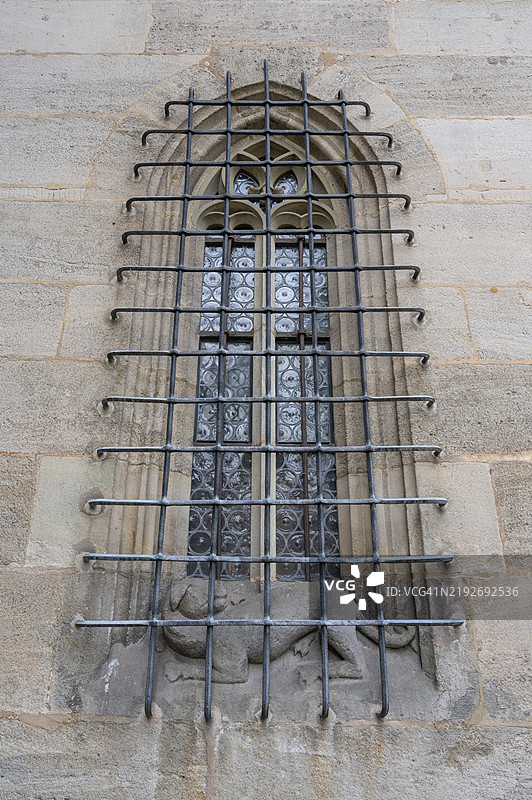 带铁栅栏的尖拱窗户，配有狗雕塑，位于德国巴伐利亚丁克尔斯比尔圣乔治教堂的晚期哥特式大厅。图片素材