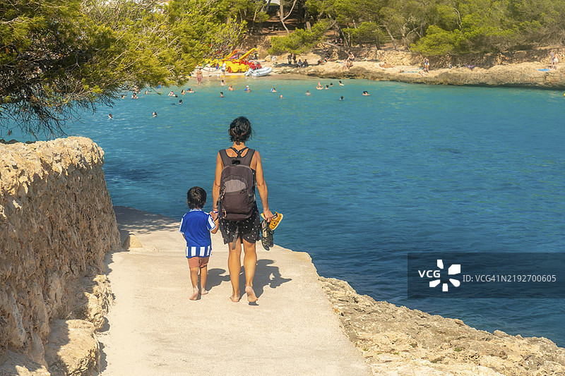 母亲和儿子赤脚走在通往西班牙马洛卡的卡拉萨马拉多尔海滩的道路上，享受夏日假期。图片素材