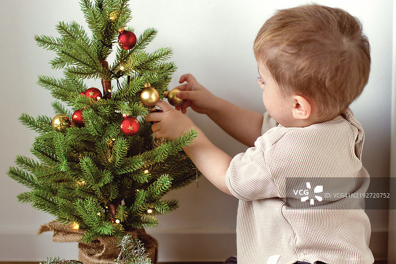 一个小孩在绿色的新年树上欣赏新年装饰。图片素材