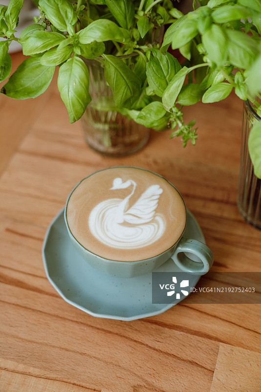 自制咖啡拿铁，杯中有天鹅拉花，配以绿松石色陶瓷杯和罗勒植物图片素材
