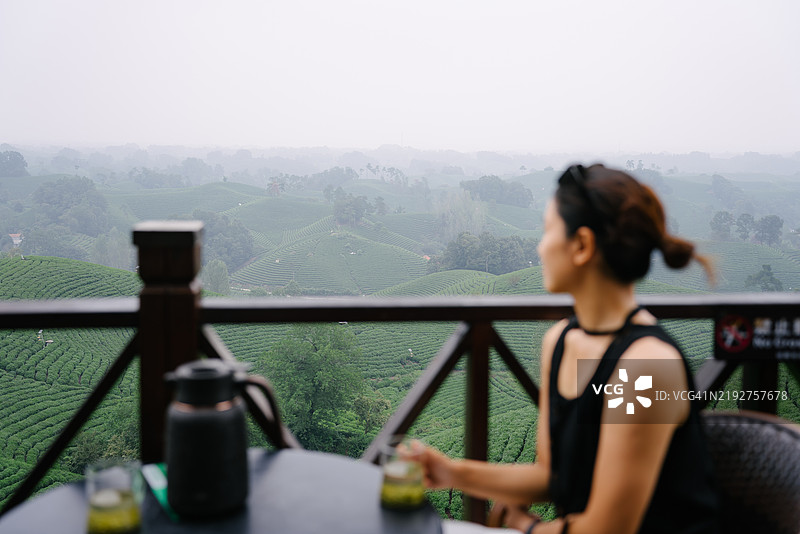 年轻的亚洲女性坐在高海拔的茶园中喝茶，这是一个绿茶生产区。图片素材