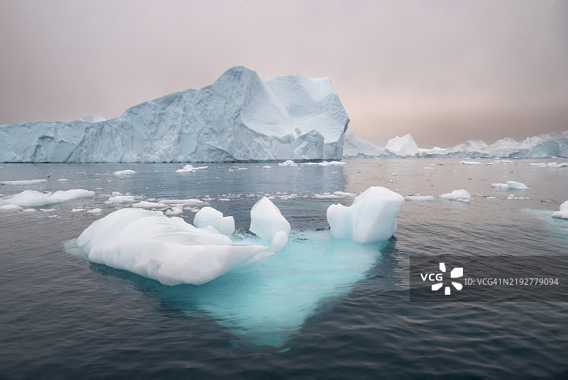 在午夜极昼的阳光季节，蓝色冰山漂浮在恶劣天气中，沉浸在雾气和美丽的迪斯科湾日落景色中。伊卢利萨特，格林兰。图片素材