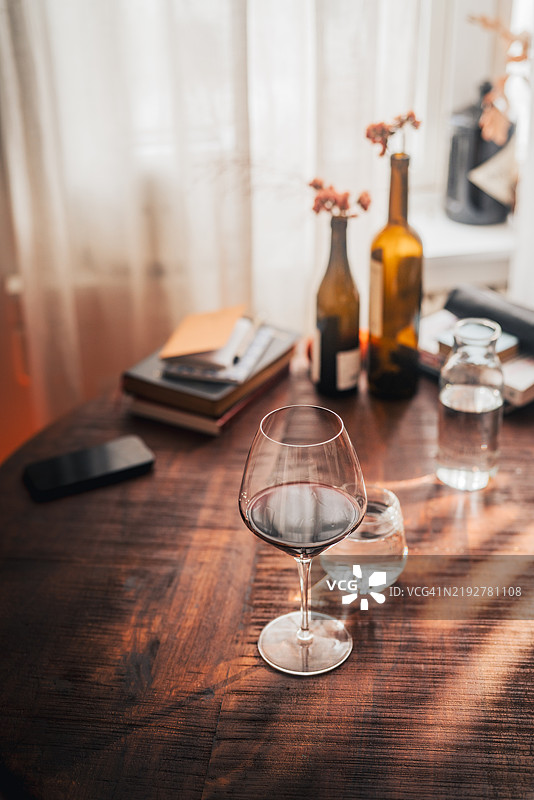 木桌上盛着红酒的酒杯，营造出温馨家庭环境中的孤独感图片素材