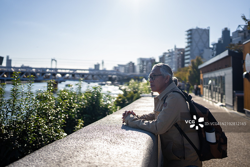 一位年长男性退休人员在隅田川岸欣赏风景。图片素材