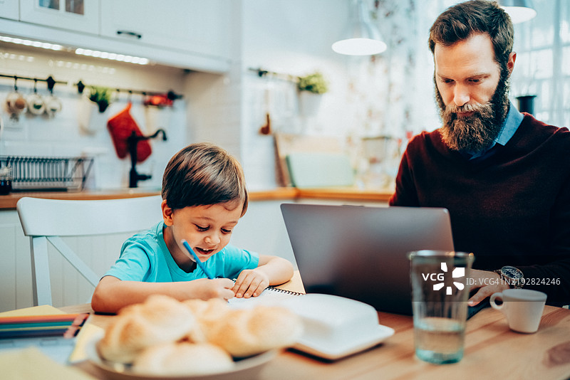 中年男子在家办公并照顾儿子图片素材