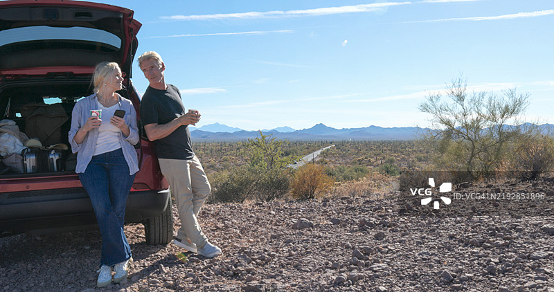成熟夫妇在沙漠中享受饮料，靠在汽车旁图片素材