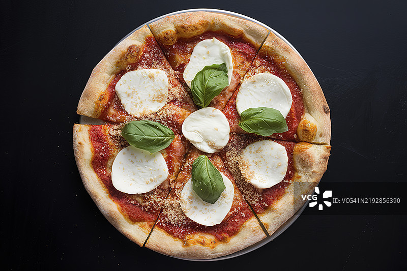 一张热腾腾、美味可口的披萨放在盘子里，背景为黑色。图片素材