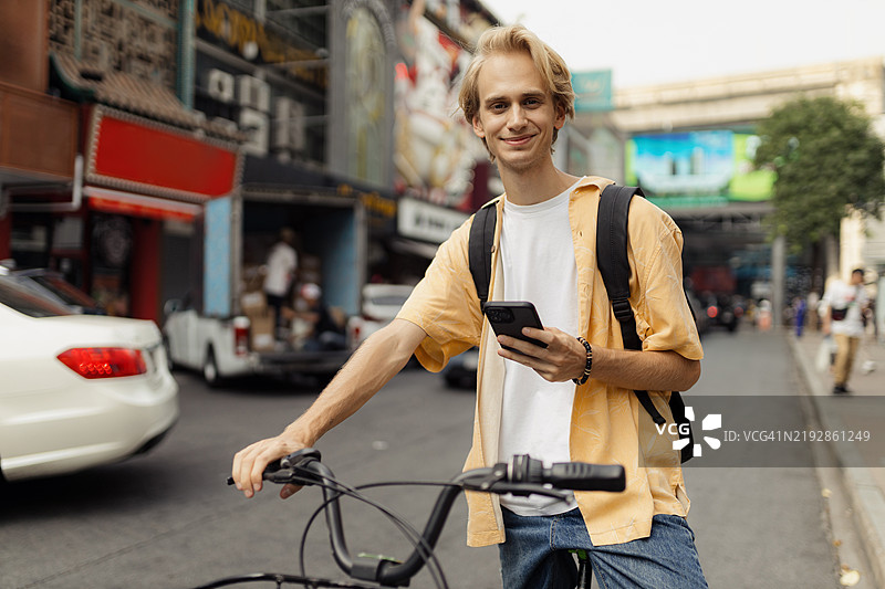 旅行者在繁忙的街道上骑自行车，享受城市冒险，手持智能手机图片素材