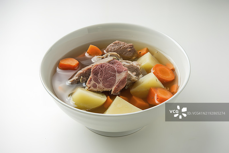 一碗白色的碗里盛着清汤，里面有肉块、土豆和胡萝卜。图片素材