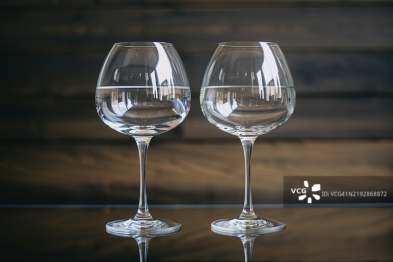 两只优雅的酒杯并排放置在深色木质背景前图片素材