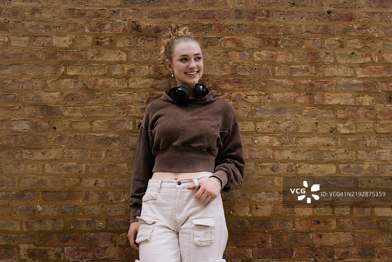 微笑的年轻女性穿着休闲服装，站在户外的砖墙前图片素材