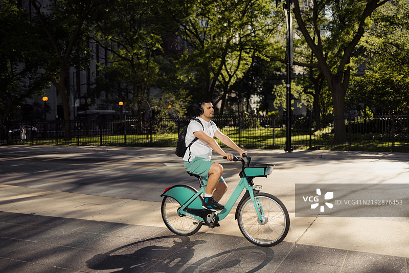 阳光明媚的下午，一名男子骑自行车穿过城市公园图片素材